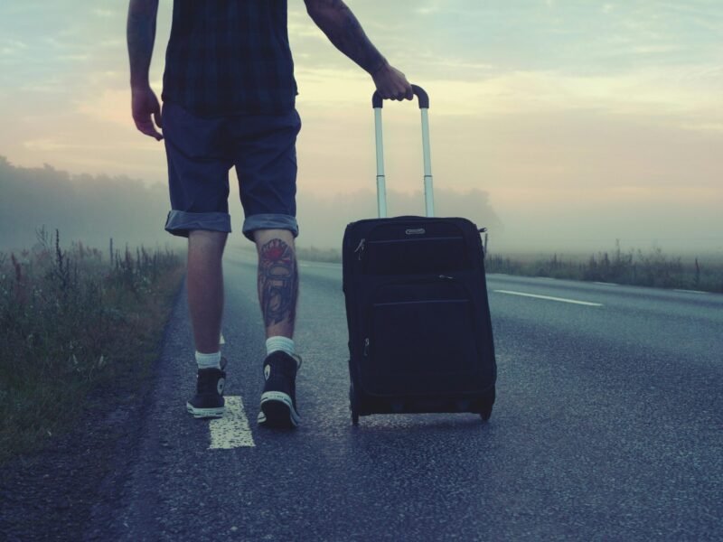 Man walking with a suitcase along a foggy road at sunrise, symbolizing adventure and travel.