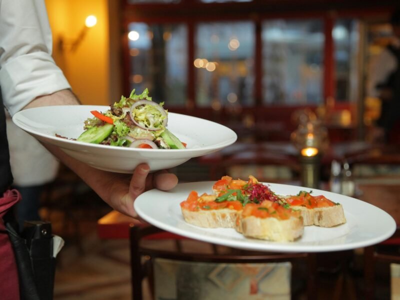 A waiter serves a fresh salad and hors d'oeuvres in a cozy restaurant setting.
