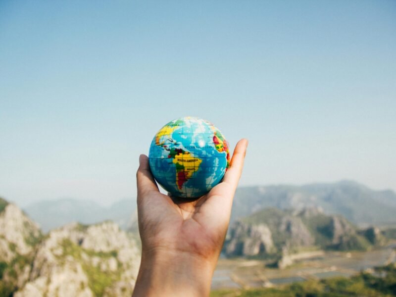 Hand holding a globe against a mountain background symbolizing travel and exploration.