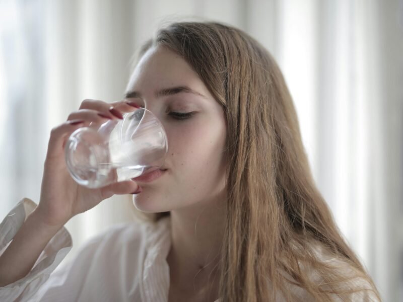 A woman enjoying a refreshing glass of water indoors during the day.